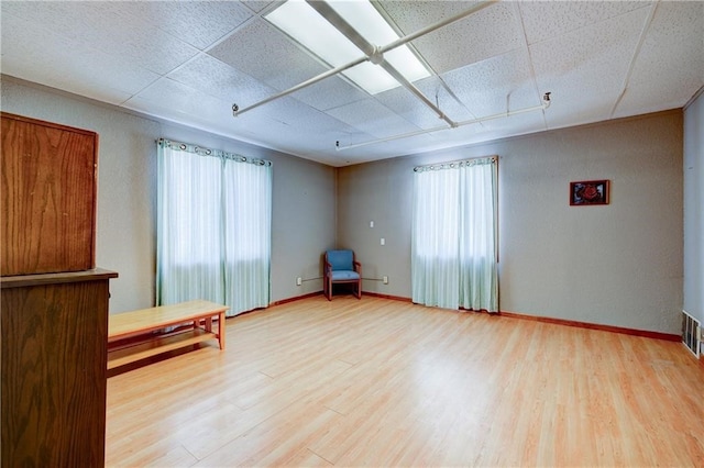 unfurnished room with plenty of natural light, wood-type flooring, and a drop ceiling