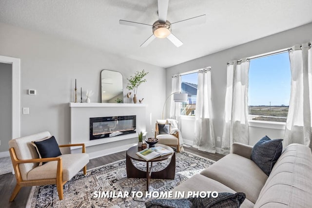 living area featuring a glass covered fireplace, baseboards, a ceiling fan, and wood finished floors