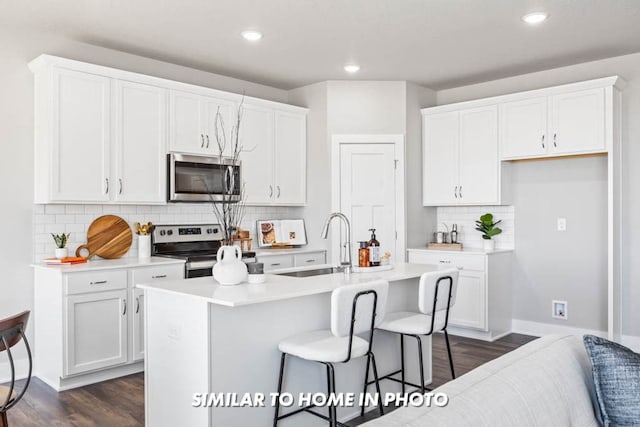 kitchen with a sink, appliances with stainless steel finishes, a kitchen island with sink, and white cabinetry