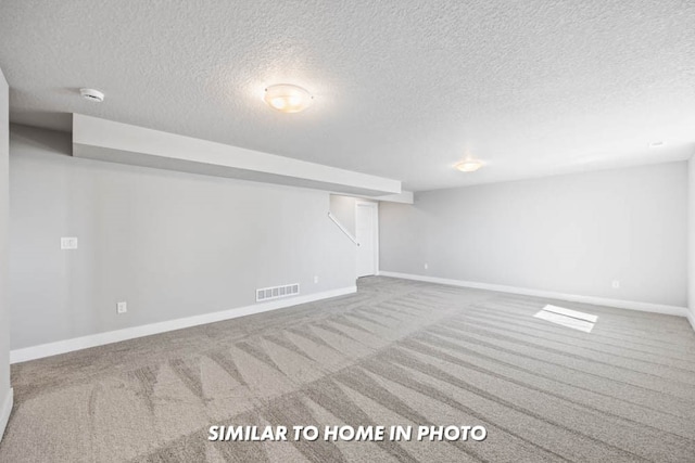 finished basement featuring visible vents, baseboards, a textured ceiling, and carpet flooring