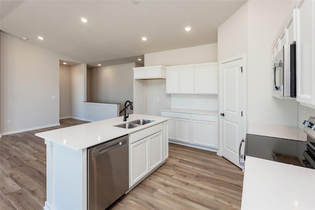 kitchen with tasteful backsplash, a sink, light wood-style floors, stainless steel appliances, and a kitchen island with sink