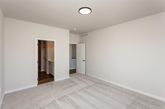 unfurnished bedroom with visible vents, baseboards, light colored carpet, and ensuite bath