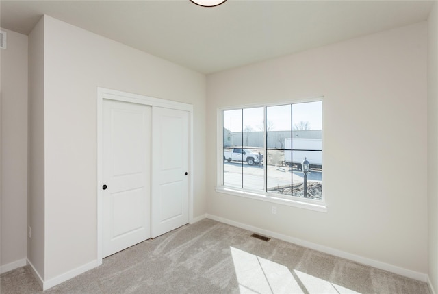 unfurnished bedroom with visible vents, baseboards, light colored carpet, and a closet