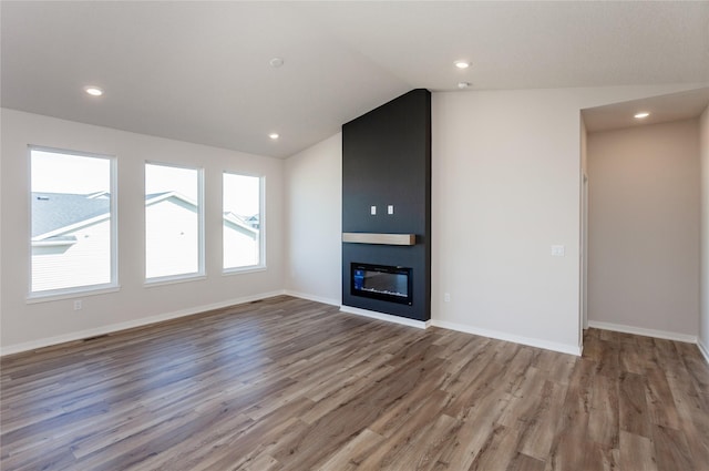 unfurnished living room featuring lofted ceiling, wood finished floors, baseboards, and a large fireplace