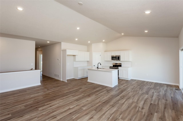 kitchen with an island with sink, a sink, open floor plan, stainless steel appliances, and light wood finished floors