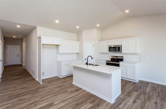 kitchen featuring a sink, lofted ceiling, stainless steel appliances, white cabinetry, and a kitchen island with sink