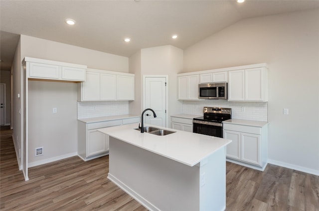 kitchen with a center island with sink, a sink, stainless steel appliances, white cabinets, and lofted ceiling