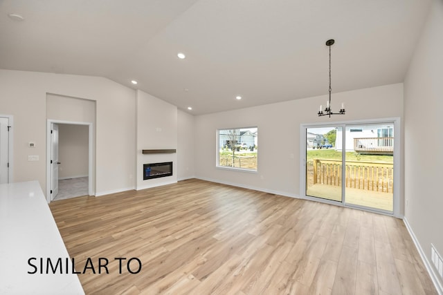 unfurnished living room with light wood-type flooring, a notable chandelier, a glass covered fireplace, and vaulted ceiling