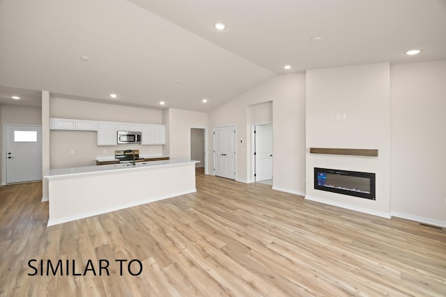 kitchen with a glass covered fireplace, light wood finished floors, lofted ceiling, appliances with stainless steel finishes, and white cabinetry