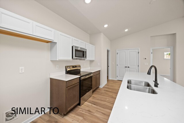 kitchen featuring lofted ceiling, a sink, light countertops, white cabinets, and appliances with stainless steel finishes