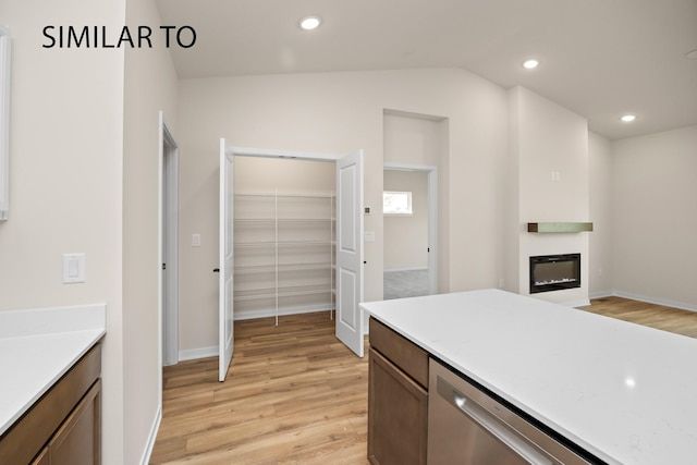 kitchen featuring a glass covered fireplace, recessed lighting, light countertops, light wood-style floors, and stainless steel dishwasher