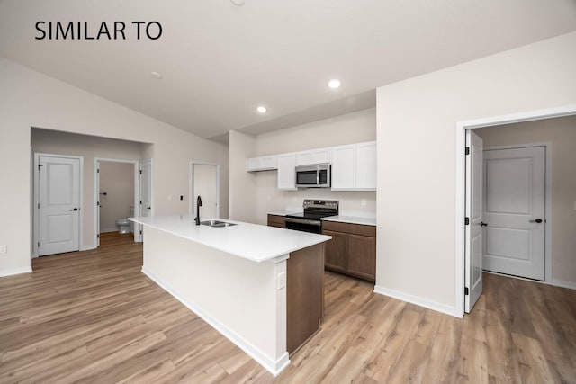 kitchen with light wood-type flooring, a kitchen island with sink, a sink, stainless steel appliances, and lofted ceiling