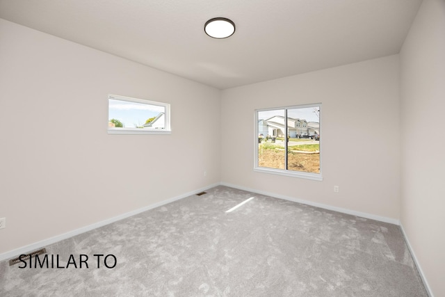 empty room featuring a healthy amount of sunlight, visible vents, carpet floors, and baseboards