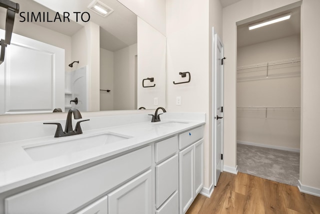 bathroom featuring a walk in closet, double vanity, wood finished floors, and a sink