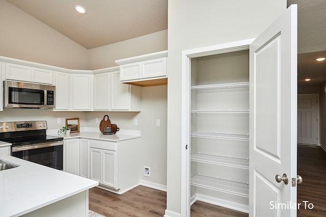 kitchen featuring hardwood / wood-style floors, lofted ceiling, white cabinetry, and appliances with stainless steel finishes