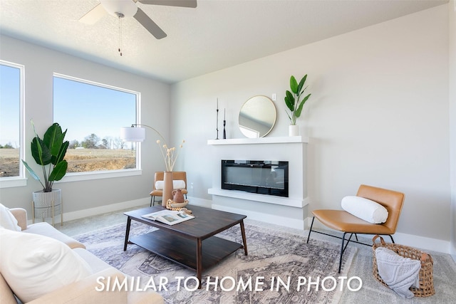 living area featuring a glass covered fireplace, a ceiling fan, and baseboards