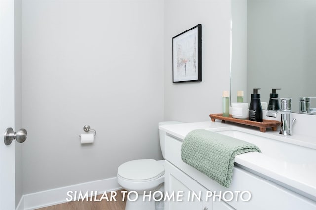 half bathroom featuring toilet, vanity, baseboards, and wood finished floors