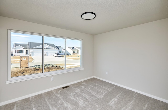 carpeted empty room with visible vents, a textured ceiling, baseboards, and a residential view