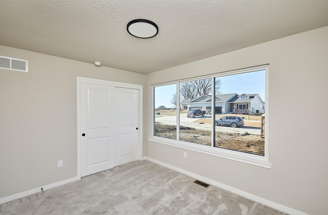 empty room with baseboards, visible vents, carpet floors, and a textured ceiling