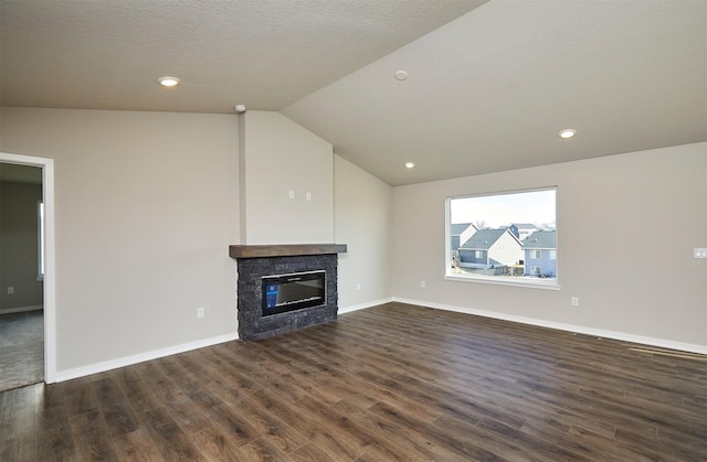 unfurnished living room featuring baseboards, vaulted ceiling, a stone fireplace, dark wood-style floors, and a textured ceiling