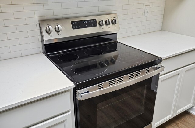 kitchen featuring stainless steel electric range oven, white cabinets, light stone counters, and tasteful backsplash