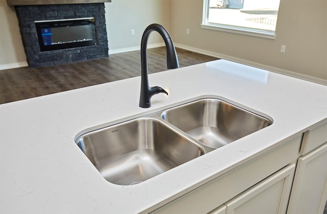 room details with a sink, baseboards, dark wood-type flooring, and a stone fireplace