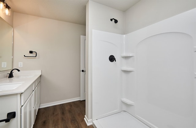 bathroom with wood finished floors, baseboards, double vanity, a sink, and walk in shower