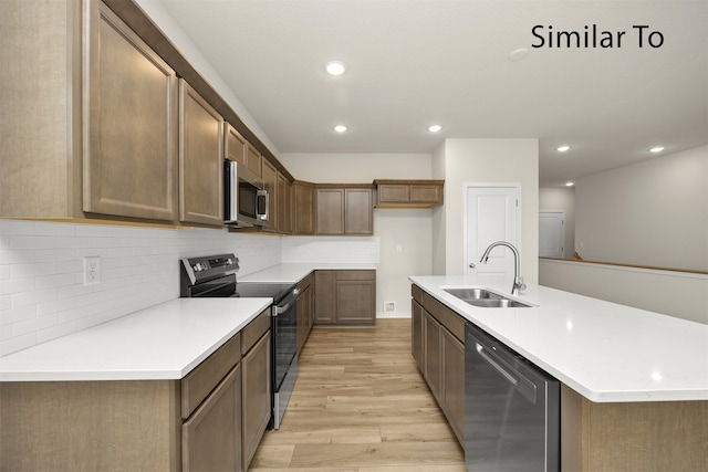 kitchen with tasteful backsplash, stainless steel appliances, a kitchen island with sink, sink, and light hardwood / wood-style floors