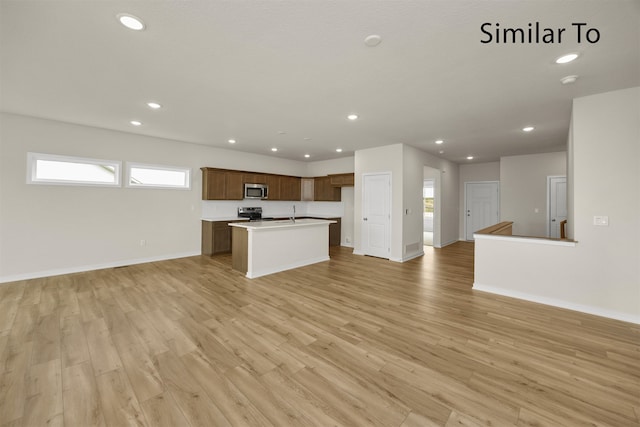 kitchen featuring appliances with stainless steel finishes, light hardwood / wood-style floors, and a center island with sink