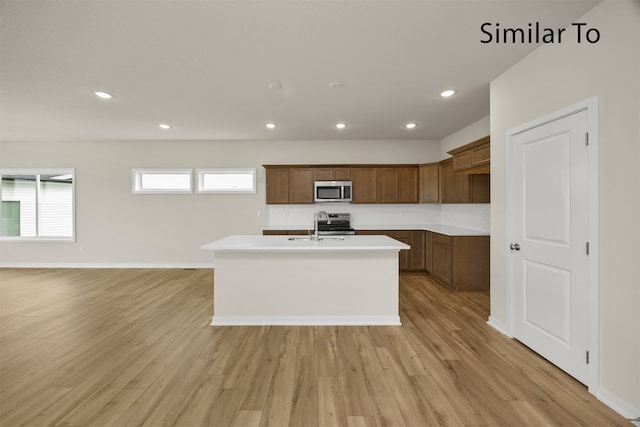 kitchen with light hardwood / wood-style floors, sink, an island with sink, and appliances with stainless steel finishes