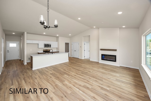 kitchen with white cabinets, sink, vaulted ceiling, light hardwood / wood-style flooring, and an island with sink