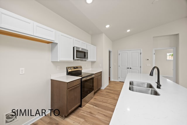 kitchen featuring stainless steel appliances, vaulted ceiling, sink, white cabinets, and light hardwood / wood-style floors