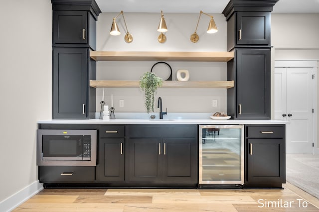 bar featuring wine cooler, sink, stainless steel microwave, and light wood-type flooring