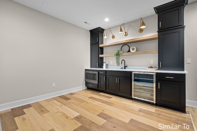 bar featuring light hardwood / wood-style floors, stainless steel microwave, sink, and wine cooler