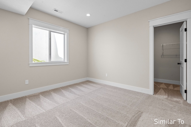 unfurnished bedroom featuring light colored carpet, a walk in closet, and a closet