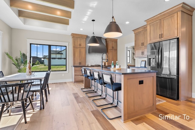 kitchen featuring hanging light fixtures, stainless steel refrigerator with ice dispenser, backsplash, a kitchen island with sink, and light wood-type flooring