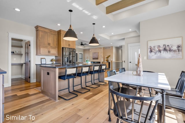 kitchen with light hardwood / wood-style floors, a raised ceiling, stainless steel fridge with ice dispenser, and hanging light fixtures