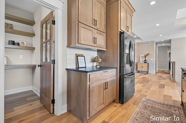 kitchen with stainless steel refrigerator with ice dispenser, a textured ceiling, light brown cabinetry, tasteful backsplash, and light hardwood / wood-style floors