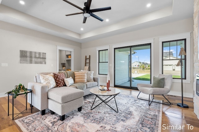 living room with ceiling fan, light hardwood / wood-style floors, and a raised ceiling