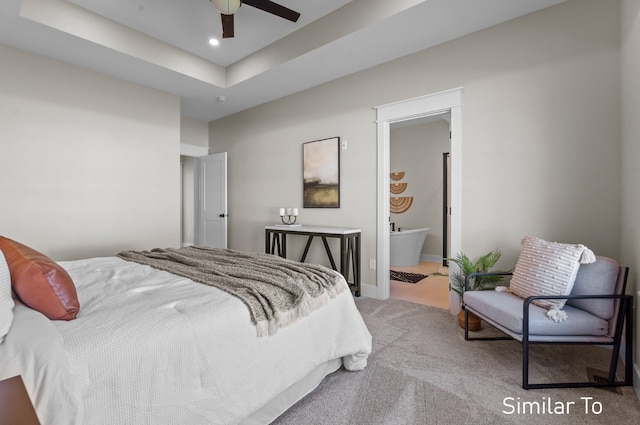 carpeted bedroom featuring ceiling fan, a raised ceiling, and ensuite bath