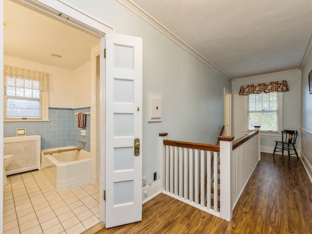 hallway with hardwood / wood-style floors, crown molding, radiator, and tile walls