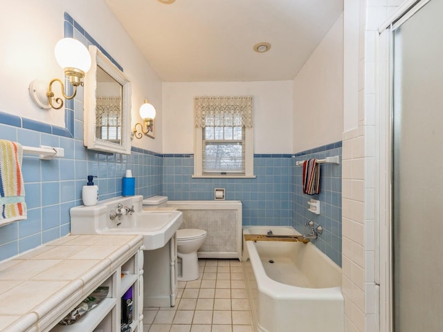 bathroom featuring radiator, tile patterned floors, toilet, tile walls, and a tub