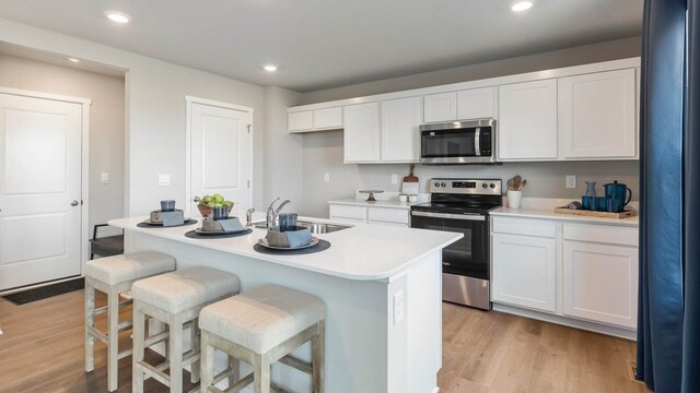 kitchen featuring light hardwood / wood-style floors, an island with sink, stainless steel appliances, white cabinets, and sink