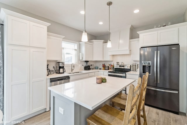 kitchen featuring white cabinets, sink, appliances with stainless steel finishes, decorative light fixtures, and a kitchen island