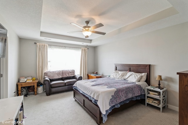 carpeted bedroom featuring a tray ceiling, ceiling fan, and a textured ceiling