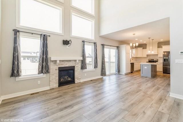 unfurnished living room with light wood-type flooring, a glass covered fireplace, baseboards, a towering ceiling, and a notable chandelier