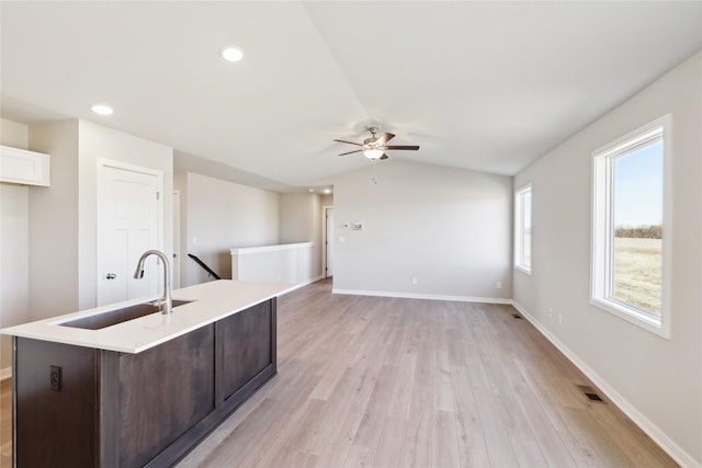 kitchen featuring lofted ceiling, sink, light wood-type flooring, ceiling fan, and a kitchen island with sink