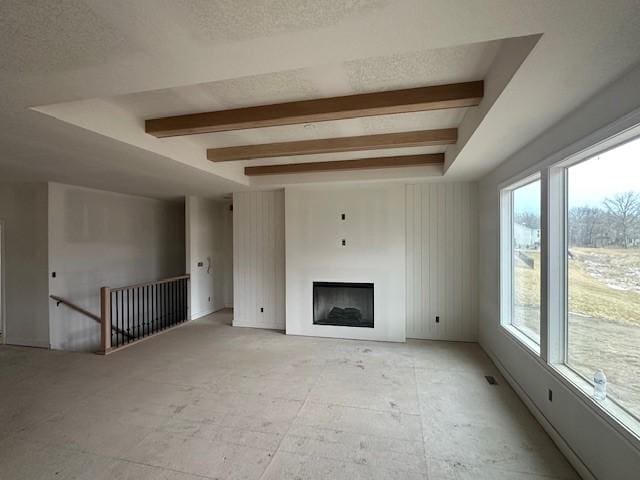 unfurnished living room with a textured ceiling, beamed ceiling, and a fireplace