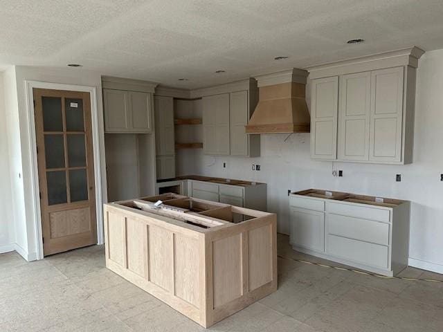 kitchen with premium range hood, baseboards, a textured ceiling, and a center island