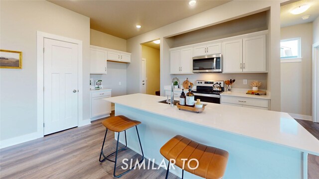 kitchen with stainless steel appliances, an island with sink, white cabinets, and a kitchen bar